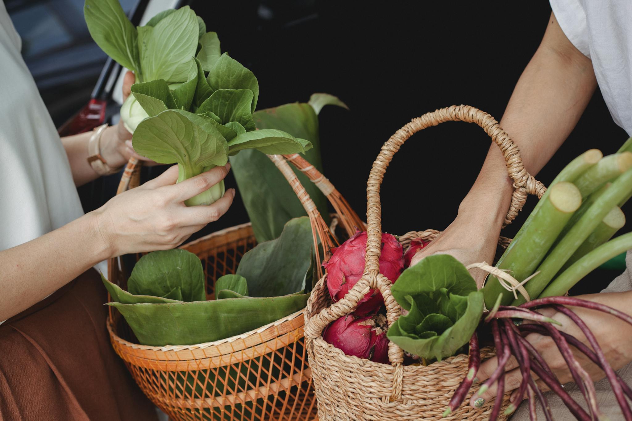 Close-up of hands holding wicker baskets filled with fresh vegetables and fruits outdoors.